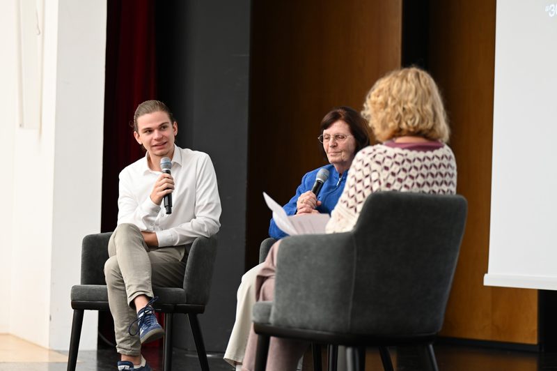 Michael Eibl und seine Oma mit Mikrofonen im Filmgespräch, im Vordergrund Moderatorin Eva Haupt von hinten